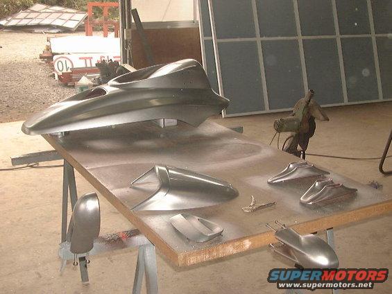 Gray car body parts on a workbench, including a large hood or roof section and smaller fender or bumper pieces